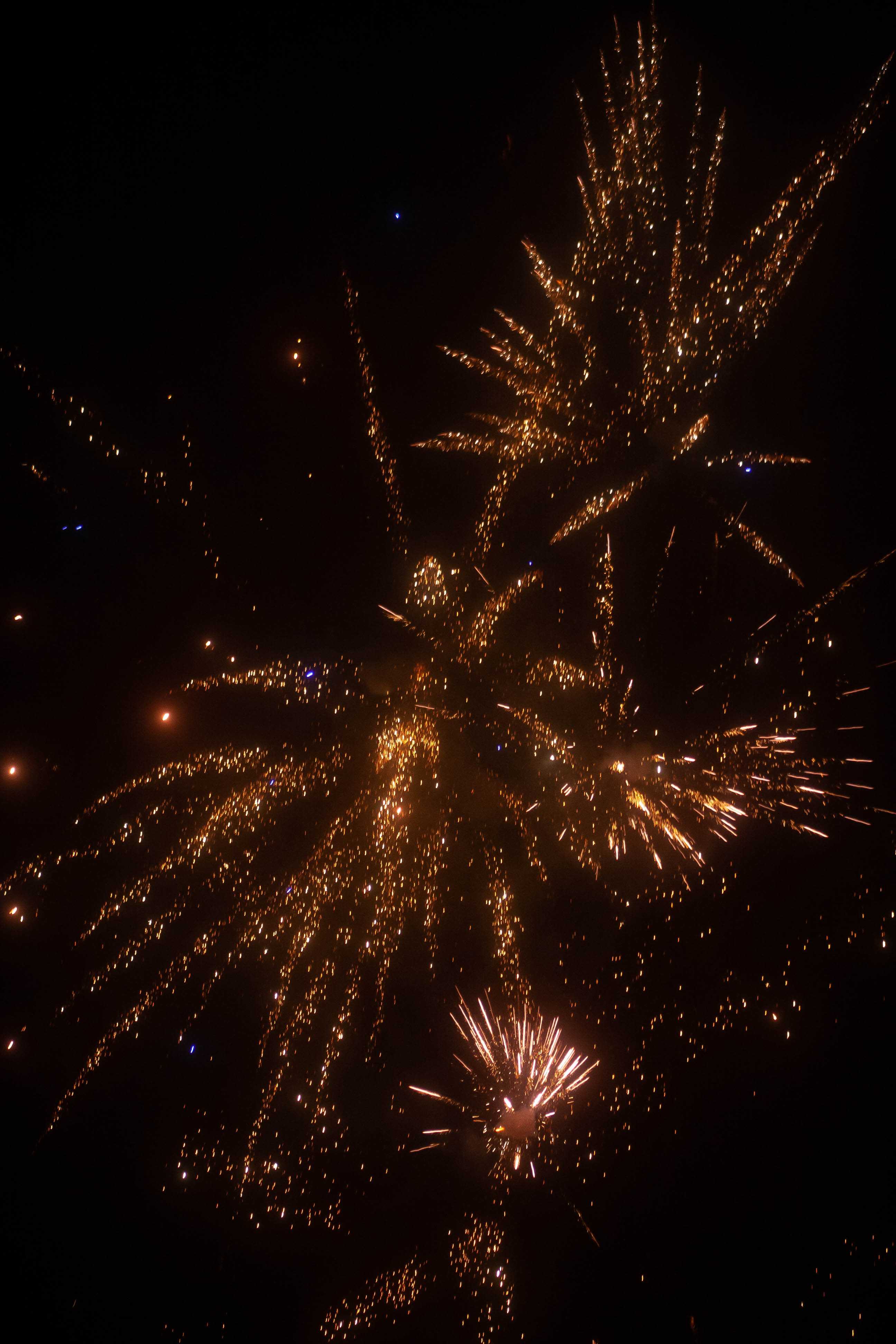 Orange colored firework sparks exploding from three different points in the image (in the middle, middle bottom and right-top corner).